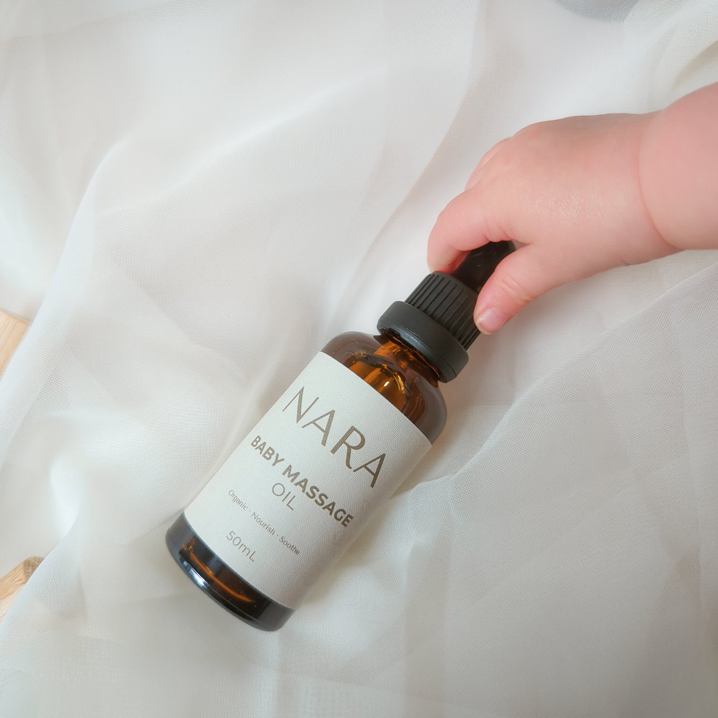 NARA Organic Baby Massage Oil held by babies hand - for soft and sensitive skin, smoothing and hydrating